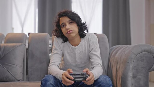 Bored Indian kid boy playing video games on controller