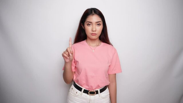 Beautiful Asian woman wearing pink shirt with hand gesture pose rejection or prohibition with copy space in Studio with White background