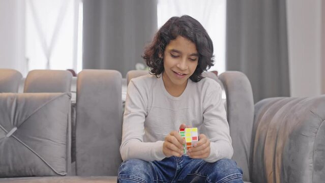 Happy Indian kid teenager boy trying to solve Rubik's cube