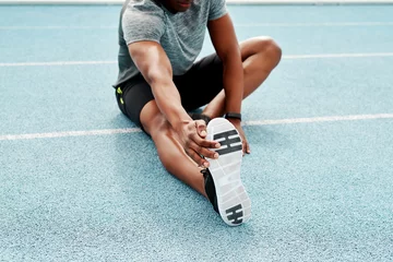 Zelfklevend Fotobehang Athlete, sitting and track for stretching legs to start training, exercise or running for fitness outdoor. Man, runner and warm up for muscle, body and wellness at stadium for race, contest or sports © Emil Lime/peopleimages.com