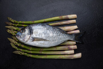 A fish on a black background with asparagus