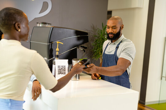 African american female customer scanning phone on bar code reader machine held by barista in cafes