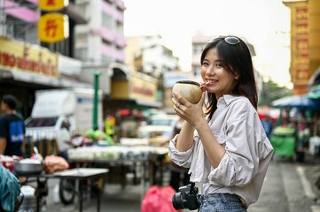 A female tourist enjoys her fresh coconut drink while walking around Chinatown's market