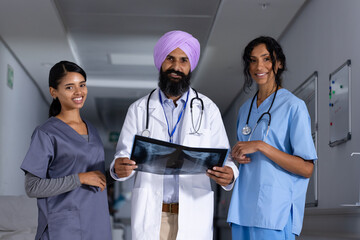 Portrait of diverse male and female doctors holding x-ray scan and smiling in corridor at hospital
