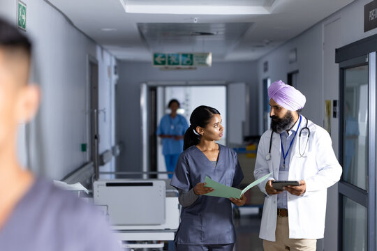 Diverse male and female doctor holding documents and discussing work in hospital corridor