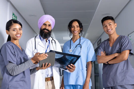 Portrait of happy diverse male and female doctors holding x-ray and tablet in corridor at hospital