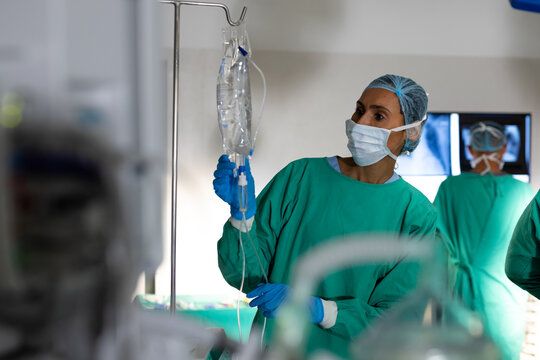 Biracial female surgeon inspecting drip bag in operating theatre at hospital