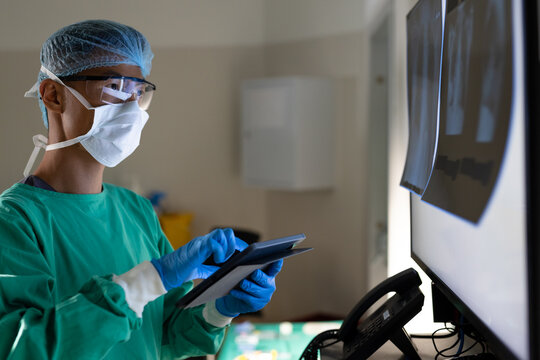 Asian male surgeon using tablet and looking at x rays in operating theatre at hospital