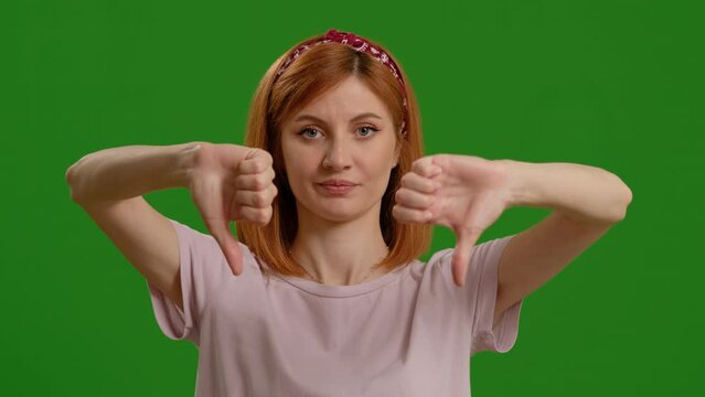 Woman, thumbs down and face by green screen for disagree, review and bad news by background. Girl, young Indian model and portrait with feedback, emoji and negative with hand sign for announcement
