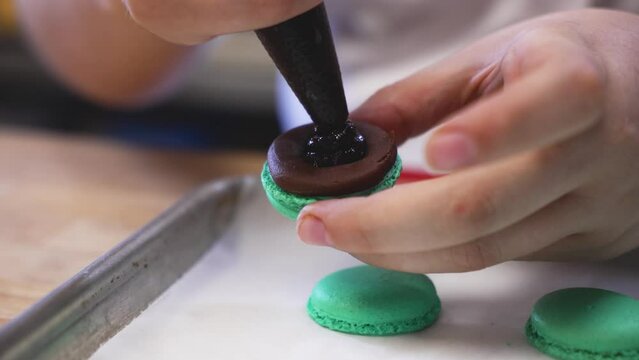 Pastry chef fills french macarons with chocolate filling, close up slow motion 4K