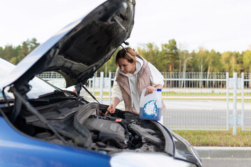 female driver checks the engine of a car with an open hood on the road