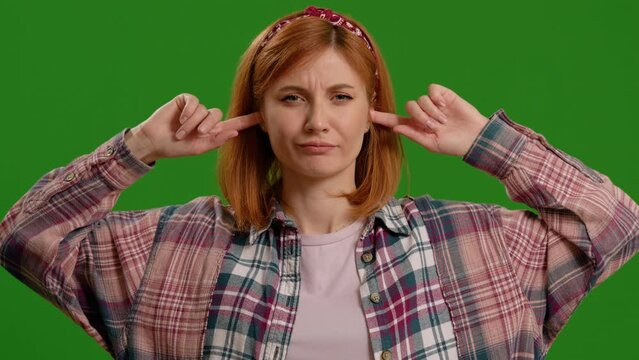 Caucasian woman hears a loud noise and covers her ears on green screen background. Female having hearing problems cannot stand loud sounds.