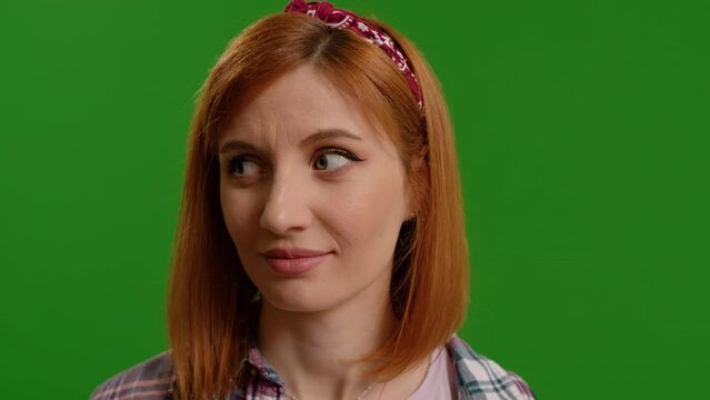 Portrait of funny young woman rolling eyes spontaniously then looking at camera on green color background. Woman grimacing childishly on camera. Emotional expressions concept.