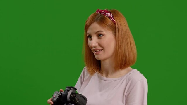 Medium shot of woman taking photos on green screen background in the studio. Female photographer using a camera taking picture while standing in the studio.