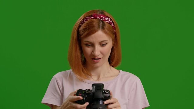Happy female photographer searching through photos with green screen background. Successful shooting day for a proffesional.