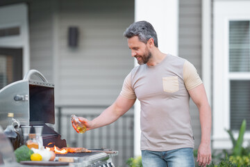 Barbecue concept. Middle aged hispanic man in t-shirt for barbecue. Roasting and grilling food. Roasting meat outdoors. Barbecue and grill. Cooking meat in backyard.