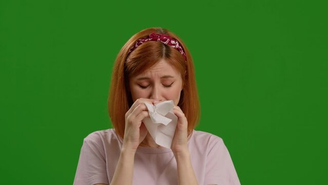Woman trying to sneeze being allergic to something holding a paper napkin to her nose over green screen background. Sick people or sad posing on camera.