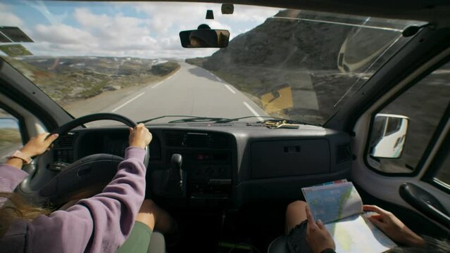 Two friends explore beautiful national park in Norway on camper van. Look at map to plan road trip, drive on small mountain road. Camper van or RV adventure concept