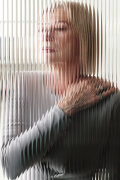 Vertical through textured glass wall portrait of elegant senior Caucasian woman with blond bob cut hair, vertical stripes distortion effect