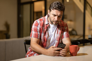 Man relaxing sitting on couch while looking at mobile phone. Mature man using smartphone to checking email at home. Man reading news on smartphone. Man talking on mobile phone.