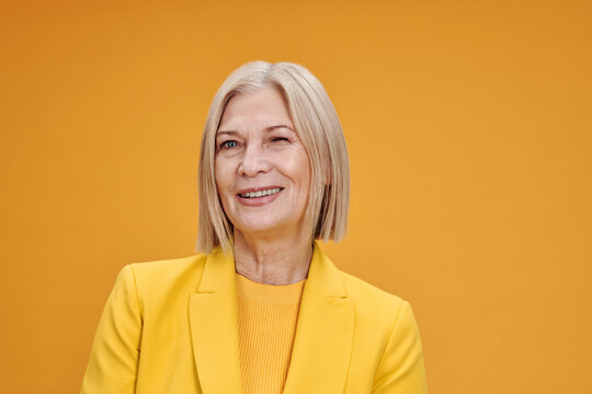 Horizontal medium close-up portrait of charming senior Caucasian woman wearing yellow clothes winking at camera, bright yellow background