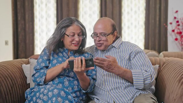 Happy Indian old couple watching funny video in mobile phone