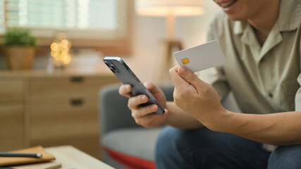 Man holding credit card and using mobile phone, making online transactions, shopping online at home