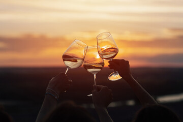 A group of girlfriends raise a toast with glasses of white wine on a sunset. Close shot.	