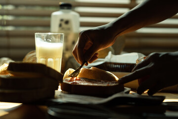 Fototapeta na wymiar Closeup shot of unrecognizable spreading raspberry jam on slice of bread with table knife