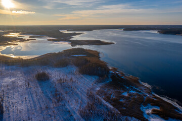 Beautiful winter landscape - drone aerial photo sunset time - frozen Wigry lake, forest and sun reflections in water and ice