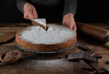 Serving a slice of cake on a cake server by womans hand on rustic, wooden and rural table background