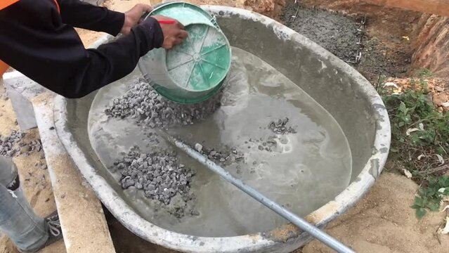 The mixing of stone, cement, sand together to make a strong concrete floor. Slow motion