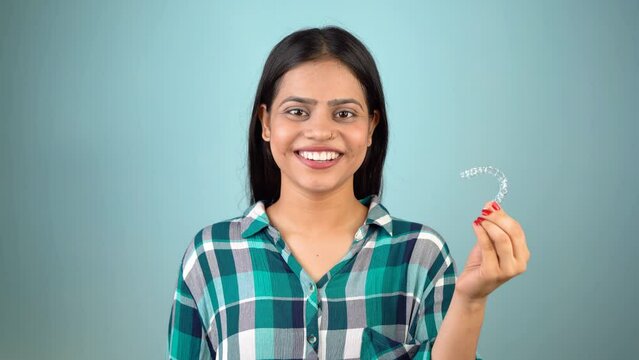 Young Asian Indian woman holding removable invisible aligner, also known as invisalign or  clear aligner