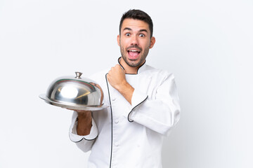 Young chef with tray isolated on white background celebrating a victory