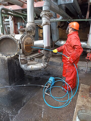Man cleaning condenser tubes removing scales of petrochemical industrial heat exchanger with high pressure water jetting machine wear helmet and protective clothing for water jetting.