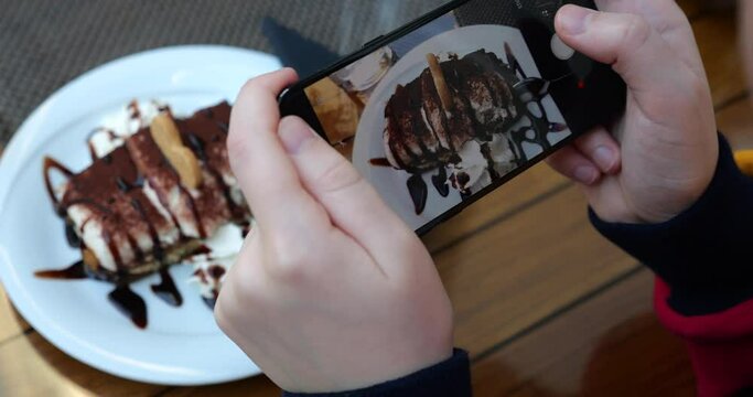 The girl chooses an angle in a smartphone for take a photo of Tiramisu dessert in cafe.