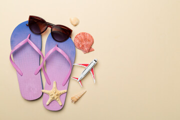 Flip flops with sunglasses and airplane on color background, top view