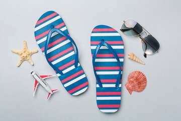 Flip flops with sunglasses and airplane on color background, top view