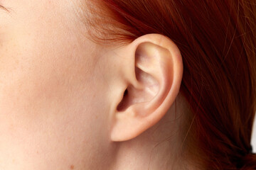 Cropped portrait with ear of young girl, woman, girl with red hair over white background. Close up image. Plastic surgery. Earlobe correction