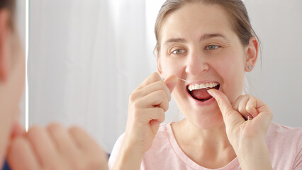 Closeup portrait of young woman using dental floss to clean her teeth. Concept of teeth health,...