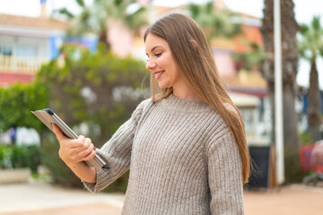 Fototapeta premium Young pretty blonde woman holding a tablet at outdoors with happy expression