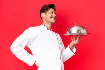 Young caucasian chef man holding tray isolated on red background suffering from backache for having...