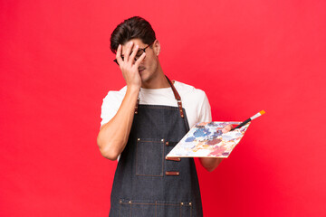 Young artist caucasian man holding a palette isolated on red background with tired and sick expression