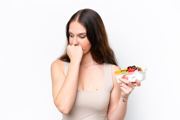 Young caucasian woman holding a bowl of fruit isolated on white background having doubts