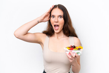 Young caucasian woman holding a bowl of fruit isolated on white background with surprise expression