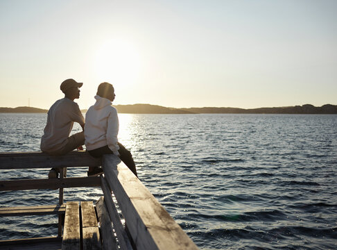 Young man and girl sitting on jetty during sunset