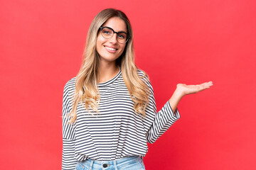 Young Uruguayan woman isolated on red background holding copyspace imaginary on the palm to insert an ad