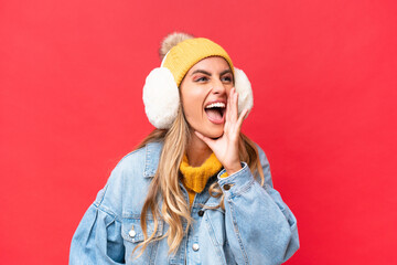 Young pretty Uruguayan woman wearing winter muffs isolated on red background background shouting...