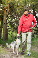 A guy in a red jacket walks his dog in the woods