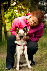 Woman hugging dog in forest. Cheerful lady in pink jacket hugs puppy sitting on a path of the...